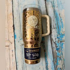 a gold colored coffee cup with a dog on the front and side is sitting on a blue wooden surface