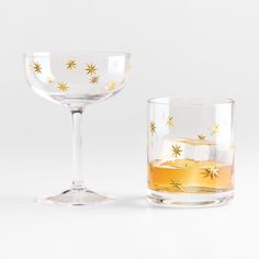 two wine glasses sitting next to each other on top of a white tablecloth with gold stars painted on them