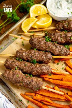 skewered meat and carrots are on a tray with lemon wedges next to it