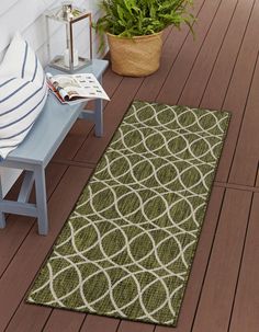 a green area rug on a wooden floor next to a blue bench and potted plant