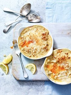 two bowls filled with food on top of a cutting board next to silverware and lemon wedges