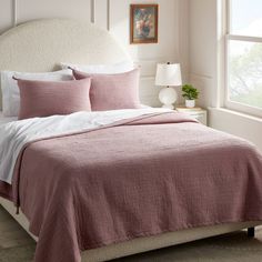 a bed with pink linens and white sheets in a bedroom next to a window