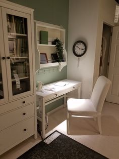 a white chair sitting next to a desk with a clock on the wall above it