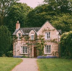 an old brick house surrounded by greenery and trees on a path leading to the front door