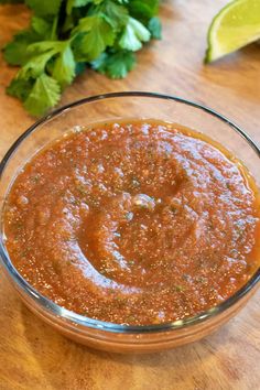 a glass bowl filled with sauce on top of a wooden table next to cilantro