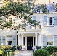 a large white house with blue shutters and trees