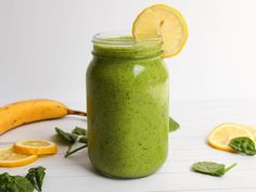 a green smoothie in a mason jar with lemons and spinach on the side