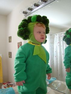 a little boy dressed in a green costume standing next to a mirror and looking at his reflection