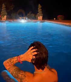 a man with his arm around his head sitting in a swimming pool at night time