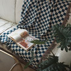 a checkered blanket on a couch next to a potted plant and a book