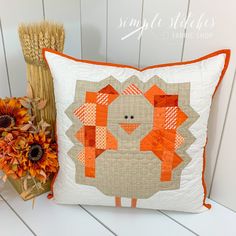 an orange and white pillow sitting on top of a table next to a vase with flowers