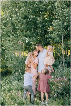 a group of people standing around each other in a field with trees and bushes behind them