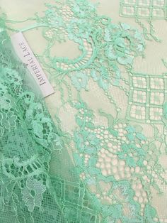 an image of green lace fabric with flowers and leaves on the bottom, as well as a tag