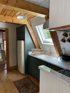 an attic kitchen with green cabinets and white walls, wood beams on the ceiling, and a rug in front of the sink