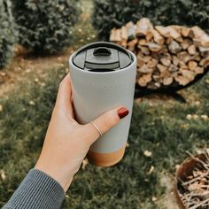 a person holding a coffee cup in their left hand while standing next to some trees