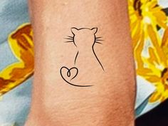 a cat's head with a heart on the left side of its wrist tattoo