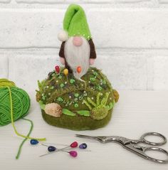 a small gnome sitting on top of a moss covered rock next to yarn and scissors