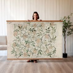 a woman holding up a large tapestry with flowers on it in front of a white wall