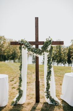 a cross decorated with greenery sits in the middle of an outdoor wedding ceremony area