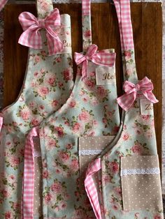 three aprons with pink and white flowers on them, one has a bow at the front