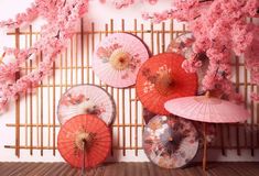 four pink umbrellas are hanging on a bamboo wall with cherry blossom trees in the background