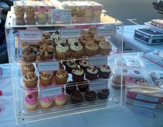 there are many cupcakes on display in the glass case at the table with other pastries