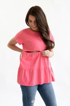 a woman wearing a pink top and jeans with her hands on her hips, smiling