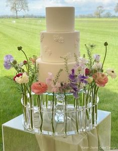 a three tiered wedding cake with pink and purple flowers in the center on a table