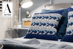 two blue pillows sitting on top of a bed next to a night stand and lamp