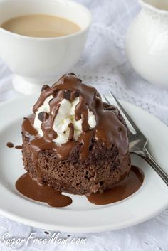 a piece of chocolate cake on a white plate with a cup of coffee in the background