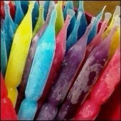 many colorful candles are lined up in a basket with water droplets on them and one candle is brightly colored