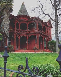 an old red house is in the middle of a grassy area with trees and bushes