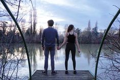 a man and woman standing on a dock holding hands looking out over a body of water