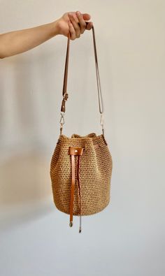 a hand holding a brown purse on top of a white wall next to a wooden handle