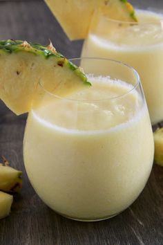 two glasses filled with pineapple juice on top of a wooden table