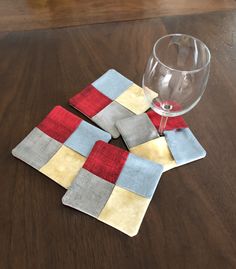 four coasters with different colored squares on them and a wine glass in the middle