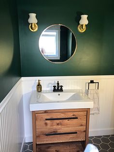 a white sink sitting under a round mirror next to a wall mounted faucet