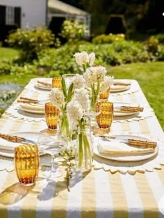 the table is set with yellow and white plates, silverware, and vases