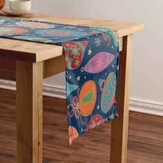 a wooden table topped with a blue and red table runner covered in christmas decorations next to a bowl of fruit