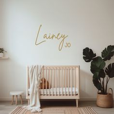 a baby's room with a crib, potted plant and name wall decal