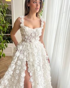 a woman standing in front of a window wearing a white dress with flowers on it