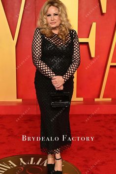 a woman in a black dress standing on a red carpet with her hands behind her back