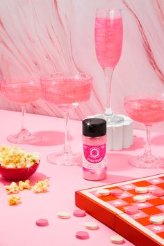 the pink table is set up with wine glasses, popcorn and other condiments