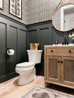 a white toilet sitting next to a wooden cabinet in a bathroom under a round mirror