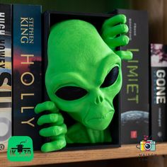 a green alien head sitting on top of a book shelf