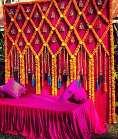 a bed covered in pink and yellow fabric with tassels hanging from the headboard