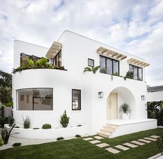 a white house with plants on the roof and stairs leading up to it's front door