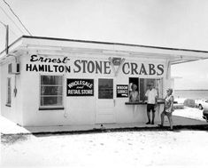 two people are standing in front of a small store with signs on the side of it