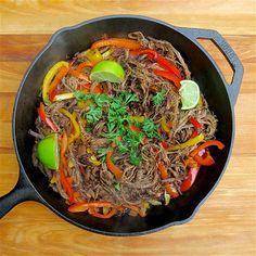 a wok filled with meat and vegetables on top of a wooden table next to a fork