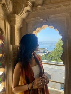 a woman standing in front of a window looking out at the ocean